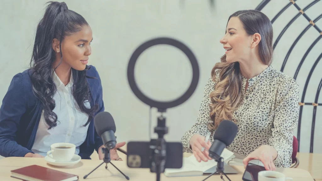 Should you have a video first podcasting strategy? Two women sit down to record a podcast with a phone recording them on video.